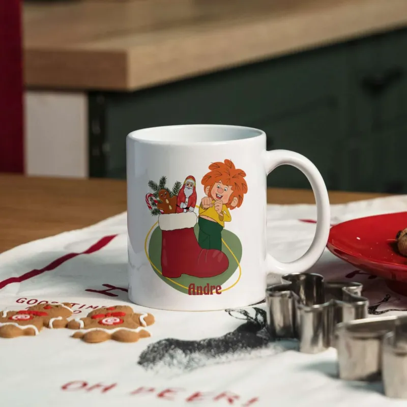Weiße ®Pumuckl Tasse Nikolaus mit Kobold im roten Stiefel und personalisierbarem Namen Andre, umgeben von Plätzchen.
